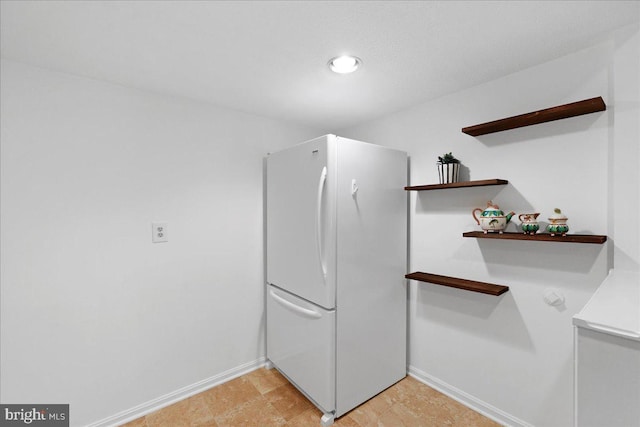 interior space featuring freestanding refrigerator, recessed lighting, open shelves, and baseboards