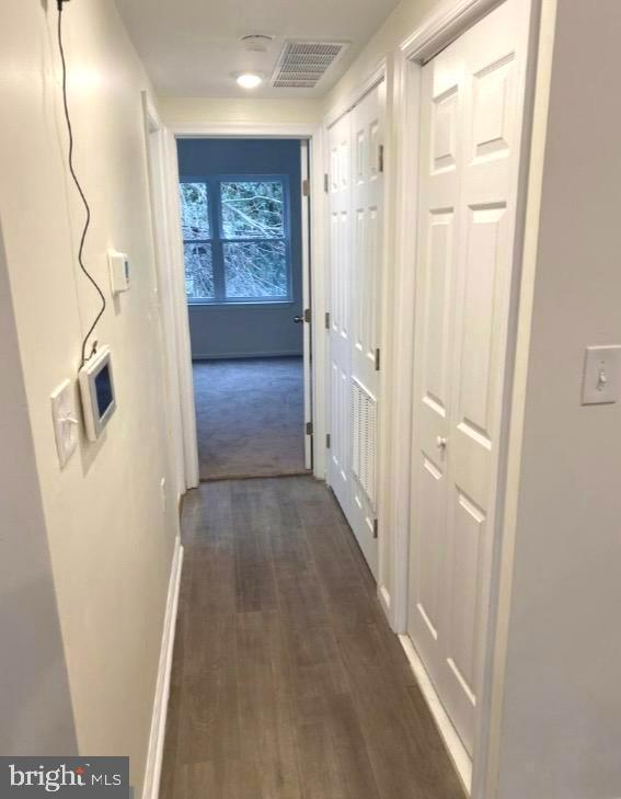 corridor featuring dark wood-style flooring, baseboards, and visible vents