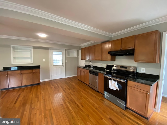 kitchen with crown molding, a sink, under cabinet range hood, light wood-style floors, and stainless steel appliances