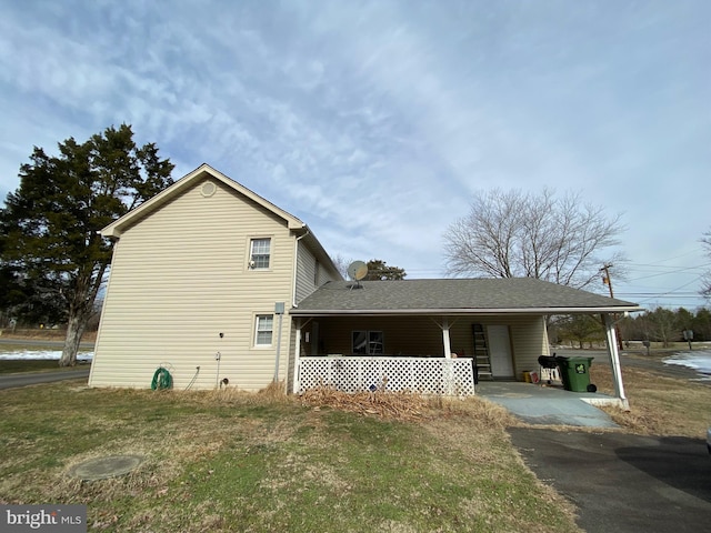 view of side of property featuring roof with shingles, a carport, a yard, and driveway