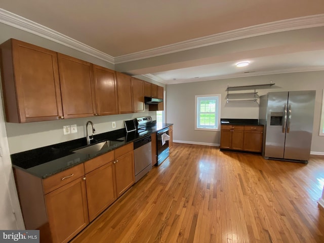 kitchen with a sink, appliances with stainless steel finishes, dark countertops, and light wood-style flooring