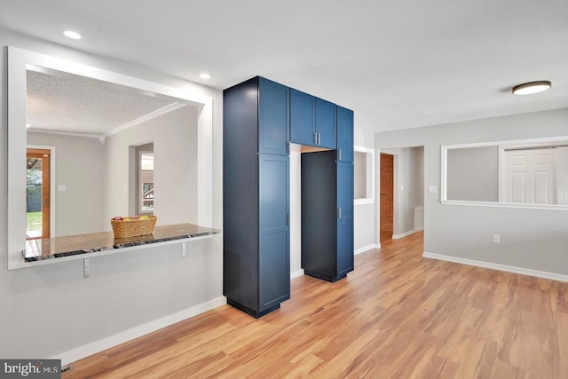 kitchen featuring crown molding, light wood finished floors, blue cabinetry, baseboards, and stone counters