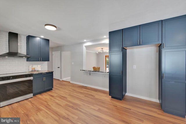 kitchen with wall chimney range hood, electric range, blue cabinetry, baseboards, and tasteful backsplash