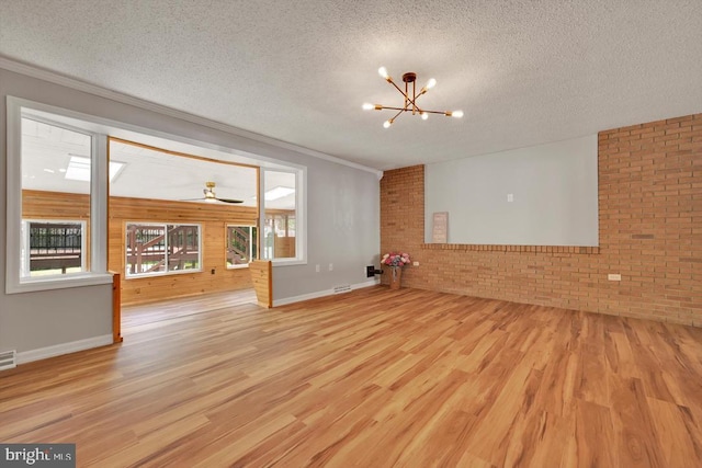 unfurnished living room with a textured ceiling, brick wall, an inviting chandelier, and wood finished floors