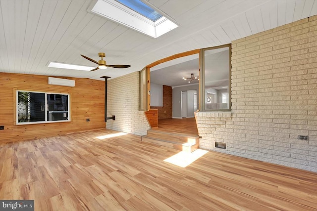 unfurnished living room with wood walls, wood finished floors, brick wall, ceiling fan, and a skylight