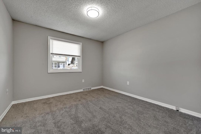 spare room with baseboards, dark colored carpet, a textured ceiling, and visible vents