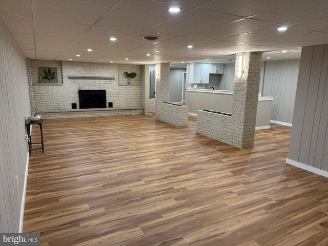 unfurnished living room with visible vents, wood finished floors, baseboards, a drop ceiling, and ornate columns