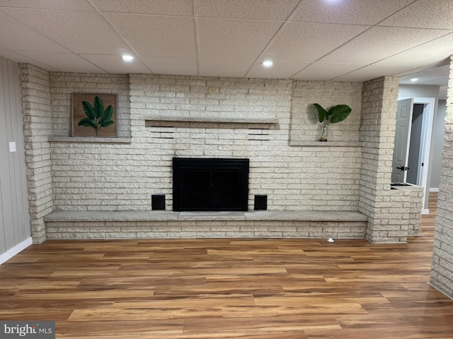 unfurnished living room with a brick fireplace, wood finished floors, baseboards, a drop ceiling, and recessed lighting