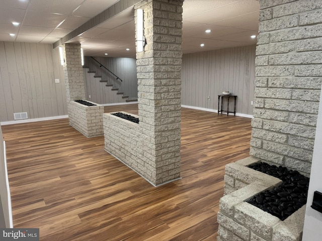 finished basement with a paneled ceiling, visible vents, wood finished floors, baseboards, and stairs