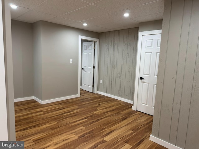 empty room featuring a paneled ceiling, recessed lighting, baseboards, and wood finished floors