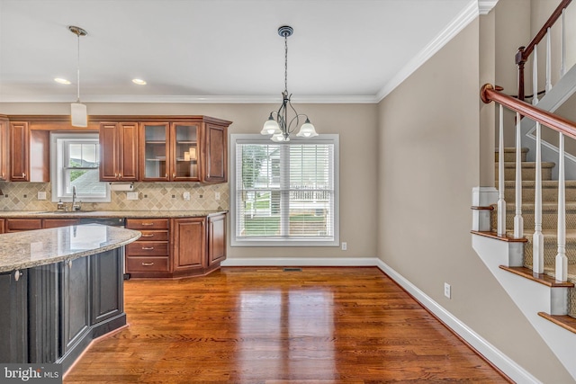 kitchen with decorative backsplash, brown cabinets, wood finished floors, light stone counters, and glass insert cabinets