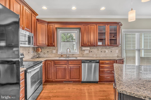 kitchen with light wood-type flooring, a sink, light stone counters, ornamental molding, and stainless steel appliances