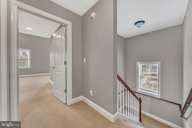 hallway featuring baseboards, light colored carpet, and an upstairs landing