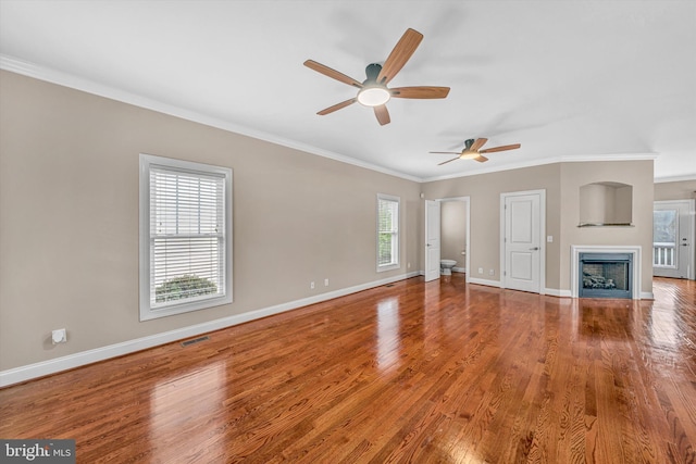 unfurnished living room with ceiling fan, visible vents, crown molding, wood finished floors, and baseboards