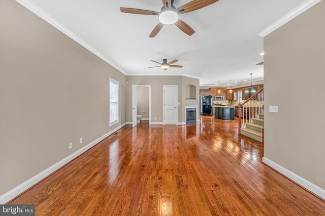 unfurnished living room featuring baseboards, ornamental molding, stairs, and ceiling fan