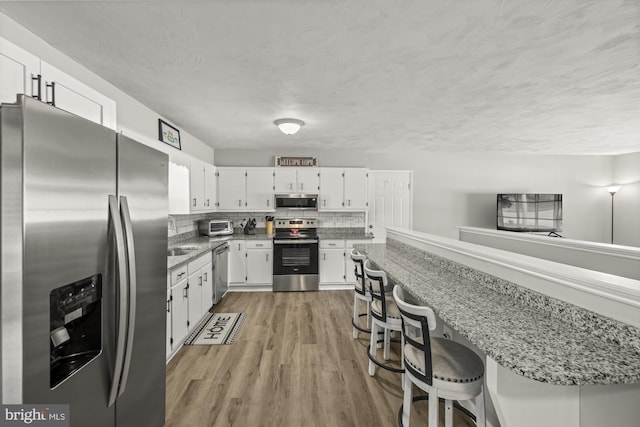 1004 Marietta Ave, Hanover, PA 17331 - kitchen featuring stainless steel appliances, white cabinets, light wood finished floors, a breakfast bar area, and light stone countertops