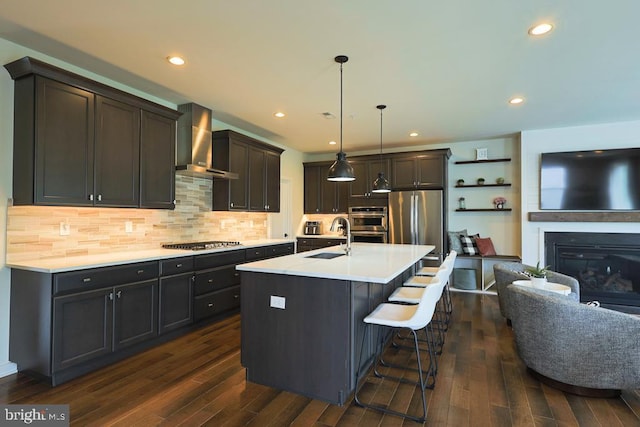 kitchen with wall chimney range hood, appliances with stainless steel finishes, dark wood-style floors, and a sink