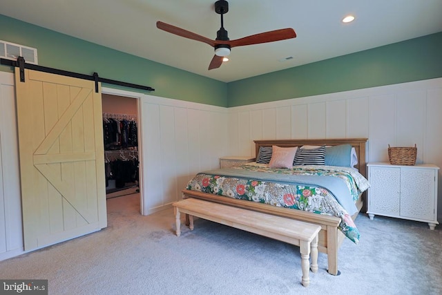 carpeted bedroom featuring visible vents, a ceiling fan, a barn door, and a spacious closet