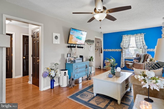 living room featuring baseboards, a textured ceiling, ceiling fan, and wood finished floors
