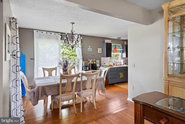 dining area with light wood-type flooring, a textured ceiling, and a notable chandelier
