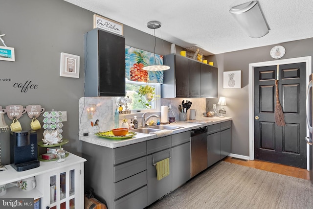 kitchen featuring stainless steel dishwasher, decorative backsplash, light wood-type flooring, light countertops, and a sink
