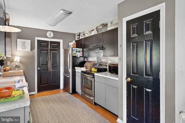 kitchen with a textured ceiling, appliances with stainless steel finishes, light countertops, light wood finished floors, and under cabinet range hood