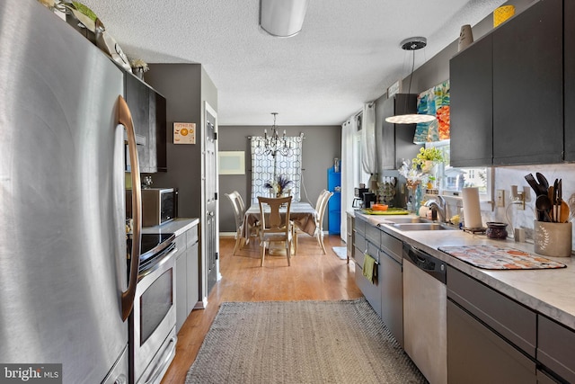 kitchen featuring a textured ceiling, appliances with stainless steel finishes, light wood-type flooring, a sink, and an inviting chandelier
