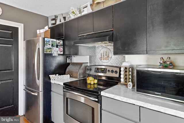 kitchen featuring light countertops, a textured ceiling, under cabinet range hood, and stainless steel appliances