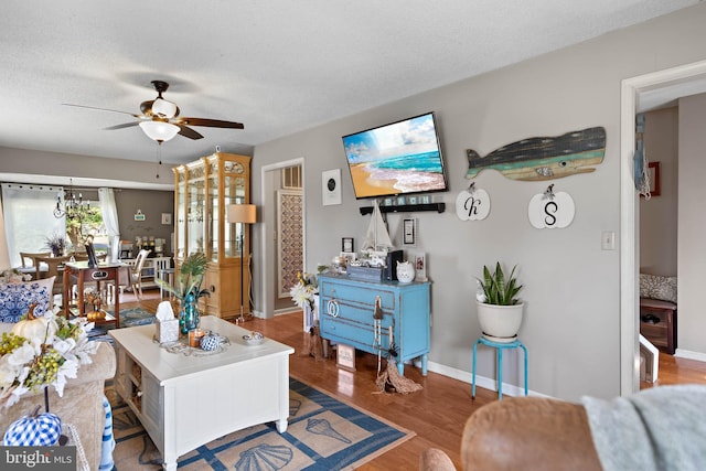 living area featuring baseboards, a textured ceiling, ceiling fan, and wood finished floors