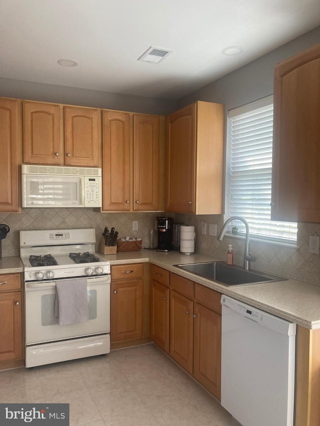kitchen with a sink, light countertops, decorative backsplash, and white appliances