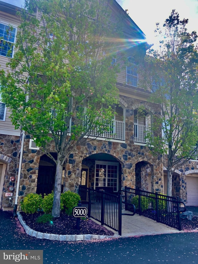 view of front of home with a porch, fence private yard, a balcony, and stone siding