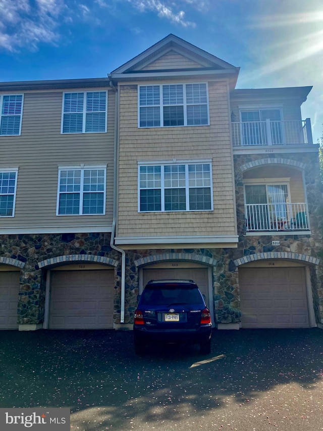 view of property featuring an attached garage, a balcony, and stone siding