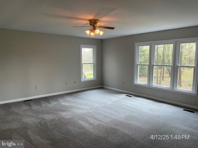 unfurnished room featuring ceiling fan, baseboards, visible vents, and dark carpet