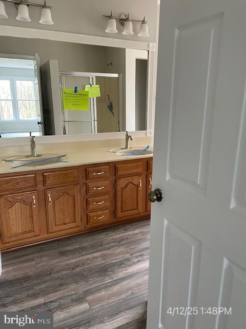 bathroom featuring wood finished floors, double vanity, a sink, and a stall shower