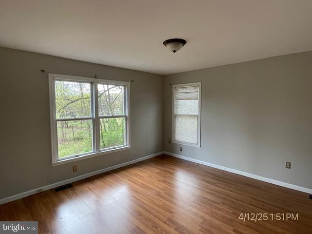 spare room with baseboards, wood finished floors, and visible vents
