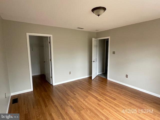 unfurnished bedroom with visible vents, a closet, wood finished floors, baseboards, and a spacious closet