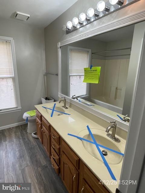full bath with a sink, toilet, double vanity, and wood finished floors
