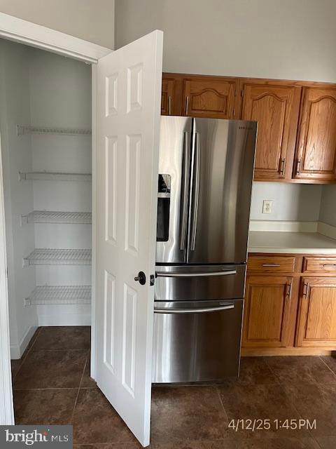 kitchen with brown cabinets, dark tile patterned flooring, stainless steel fridge with ice dispenser, and light countertops