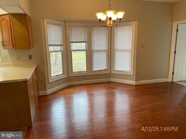 unfurnished dining area with an inviting chandelier, baseboards, and wood finished floors