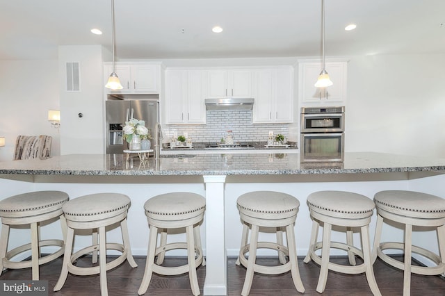 kitchen with white cabinets, stainless steel appliances, decorative backsplash, under cabinet range hood, and visible vents