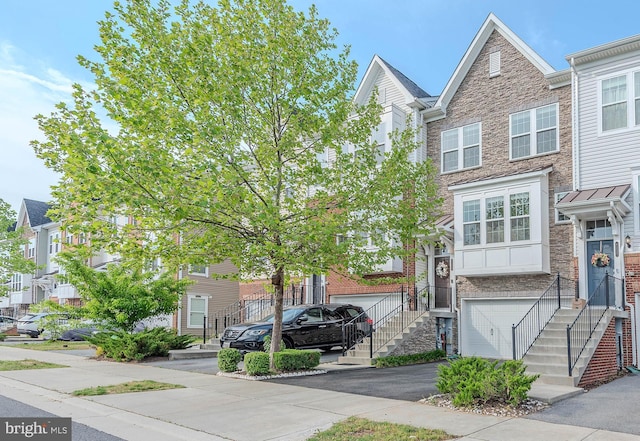 townhome / multi-family property featuring a residential view, stairs, an attached garage, stone siding, and aphalt driveway