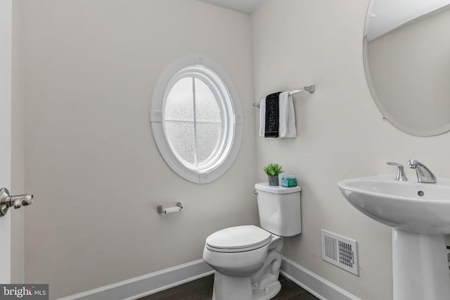 bathroom with baseboards, toilet, wood finished floors, and visible vents