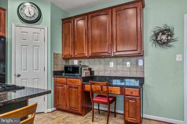 kitchen featuring stainless steel microwave, backsplash, dark stone countertops, and baseboards