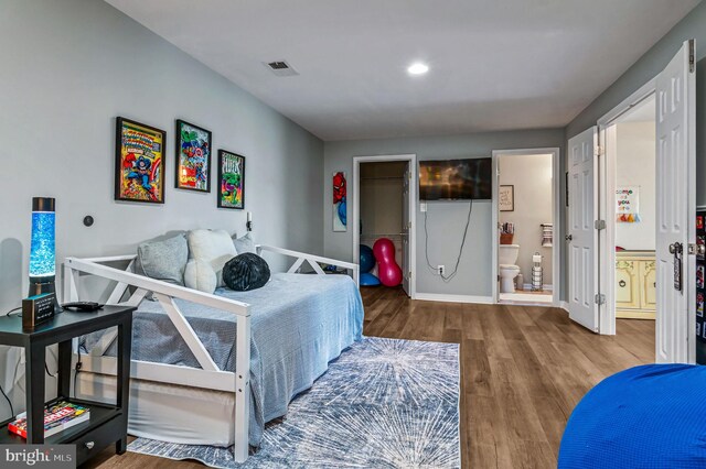 bedroom with wood finished floors, ensuite bathroom, a walk in closet, baseboards, and a closet