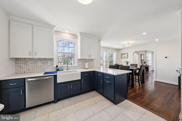 kitchen featuring tasteful backsplash, dishwasher, a sink, a peninsula, and white cabinetry