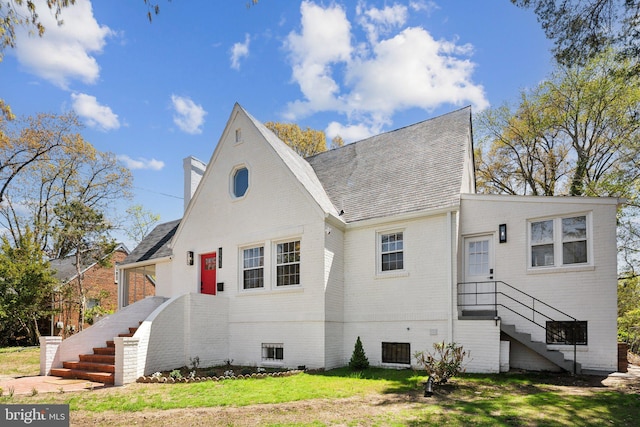 view of front facade with brick siding, a chimney, stairs, and a front yard