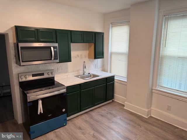 kitchen featuring appliances with stainless steel finishes, a sink, light countertops, green cabinetry, and light wood-style flooring
