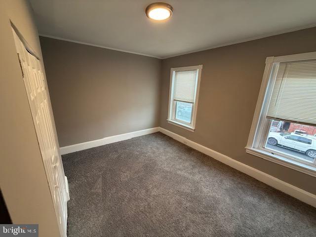 empty room featuring crown molding, baseboards, and dark carpet