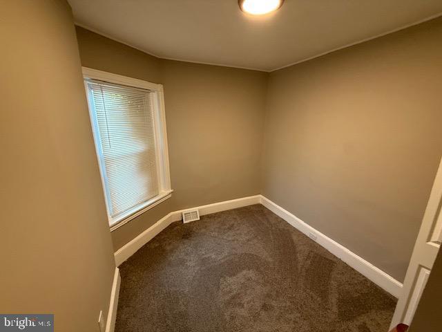 spare room with baseboards, visible vents, and dark carpet