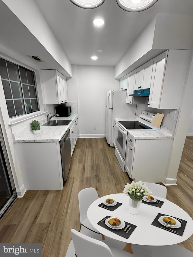kitchen with stainless steel dishwasher, white electric range, a sink, light wood-style floors, and under cabinet range hood